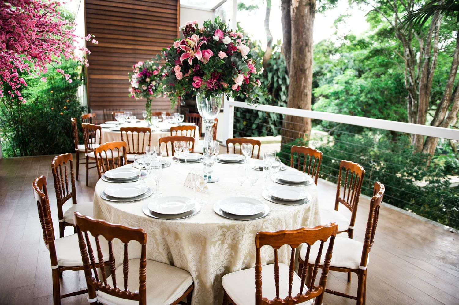 Outdoor wedding dining area with cherry blossom centerpieces and wooden chairs.