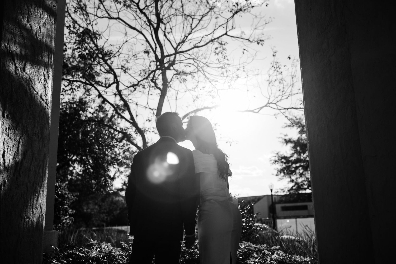 Silhouetted couple embraces against dramatic sunset through trees.