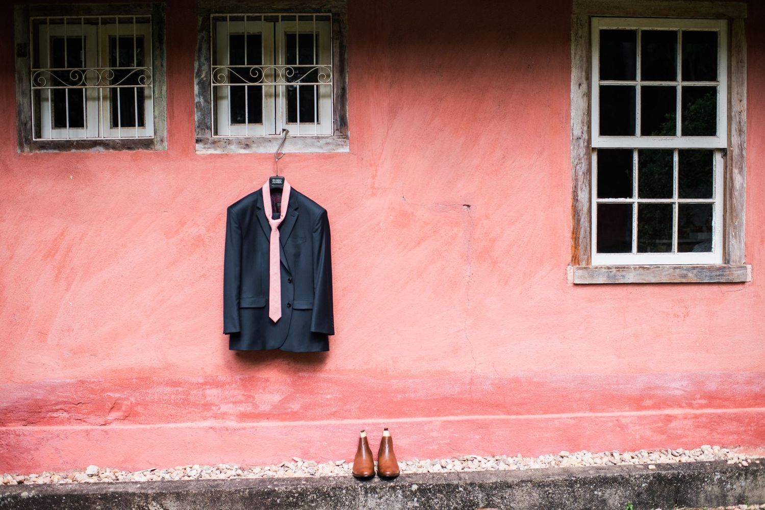 Pink stucco wall with white-framed windows and formal attire hanging.