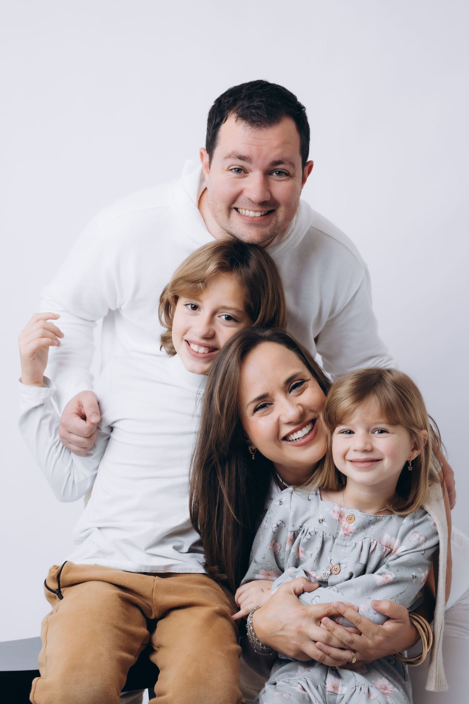 Happy family portrait session with parents and children in white and tan outfits.