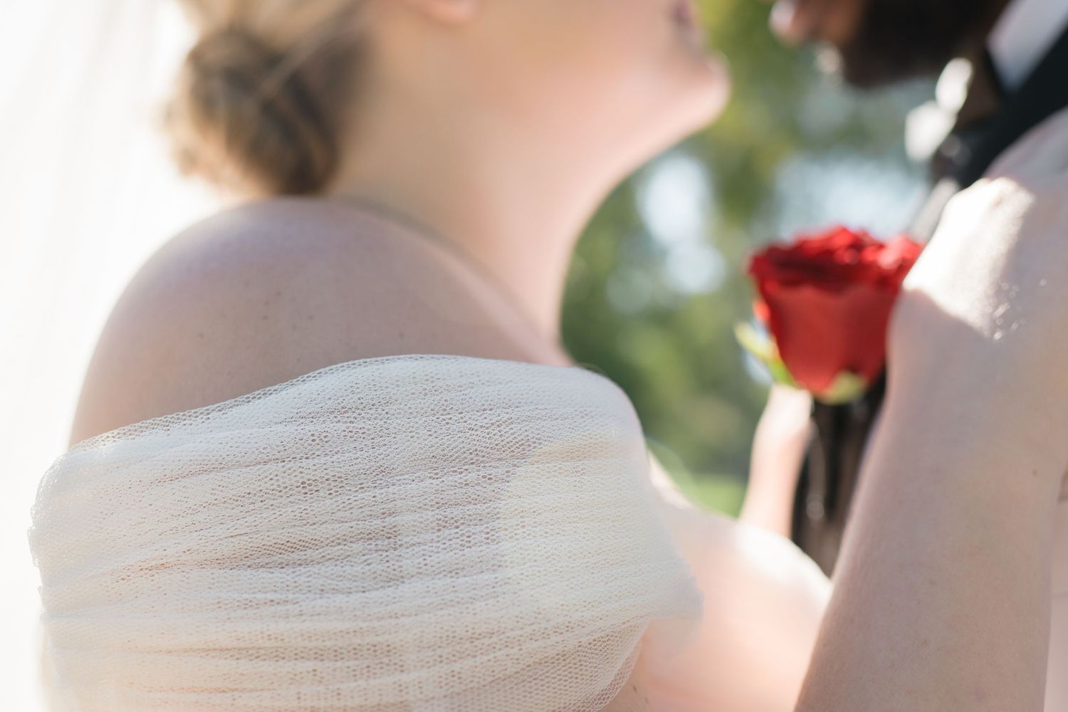 Close-up detail of white wedding dress fabric and red rose.