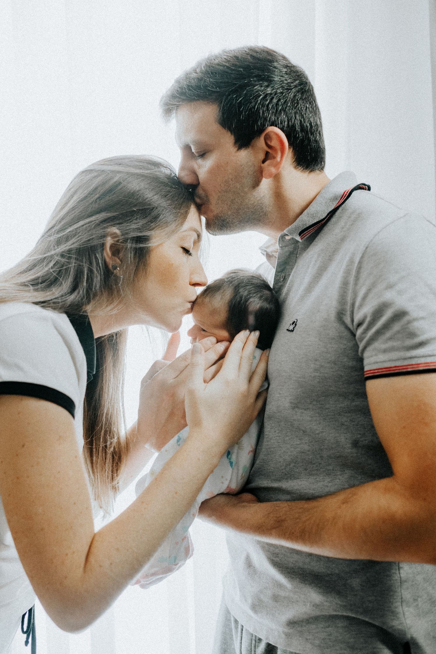 Tender family moment captured in soft lighting against a white background.