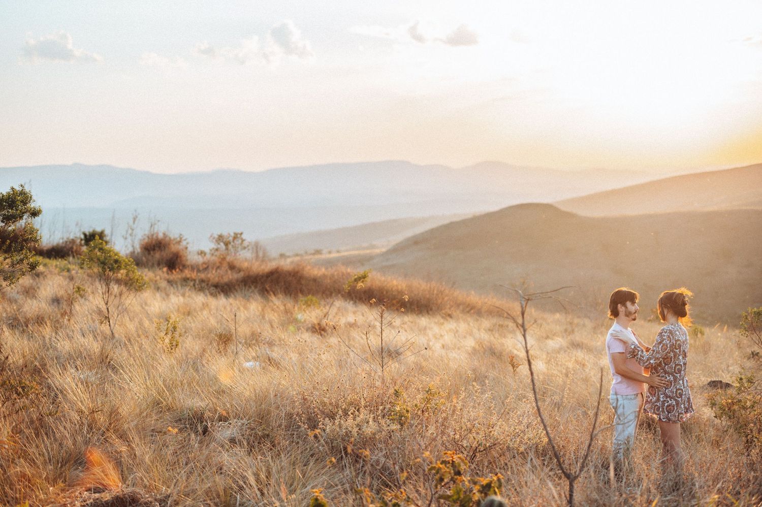 Panoramic view of couple walking through golden mountain landscape at sunset.