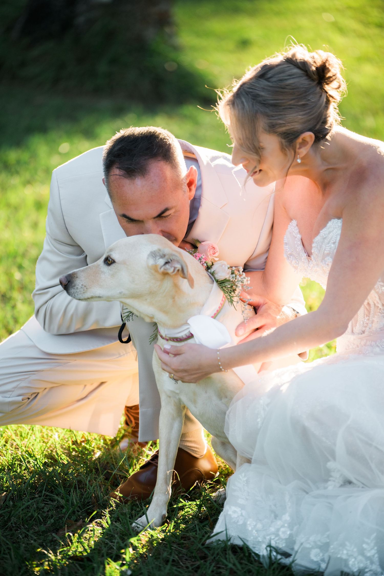 Sweet moment shared with a white dog during outdoor wedding photoshoot.