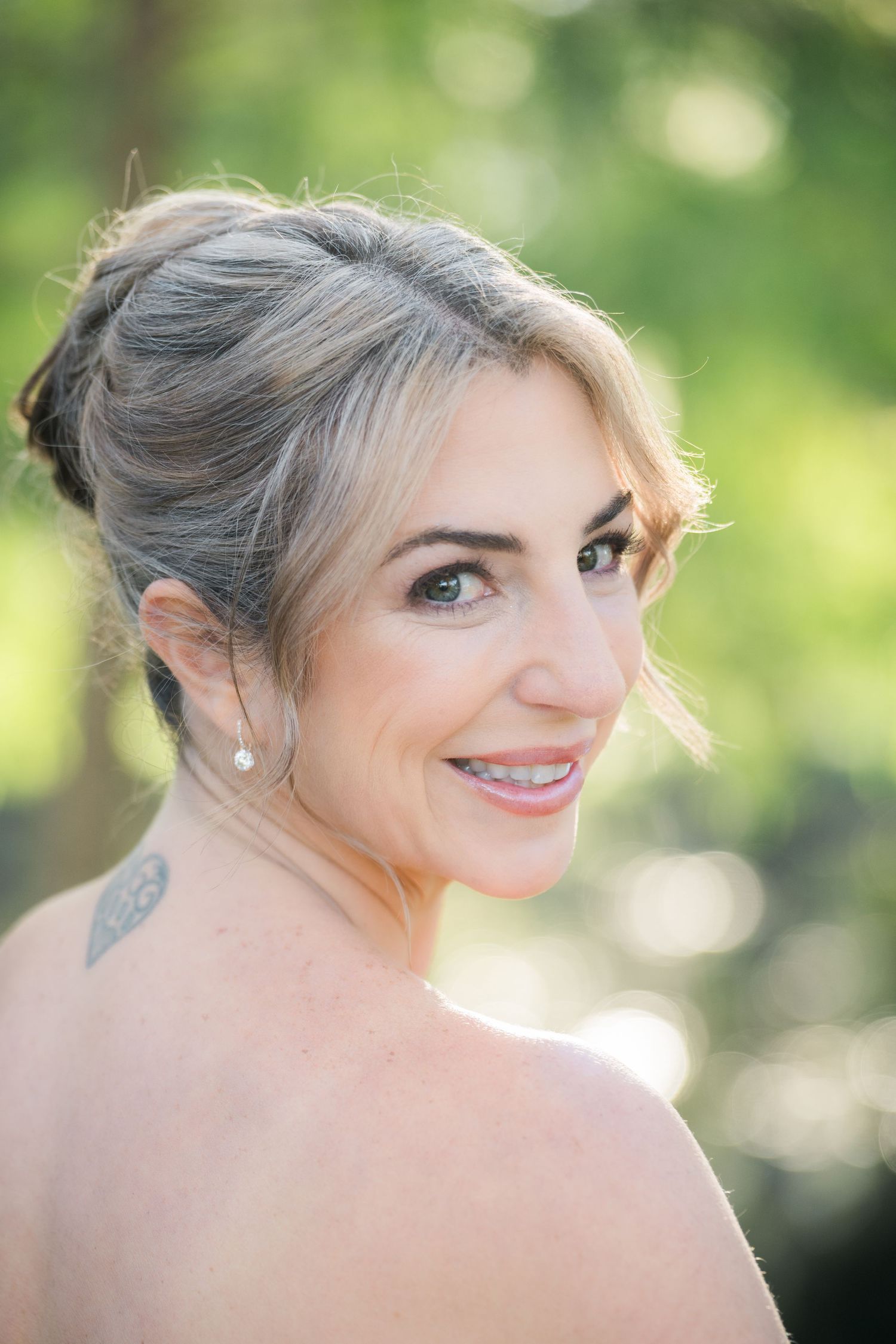 Bride with elegant updo hairstyle smiles in natural outdoor lighting.