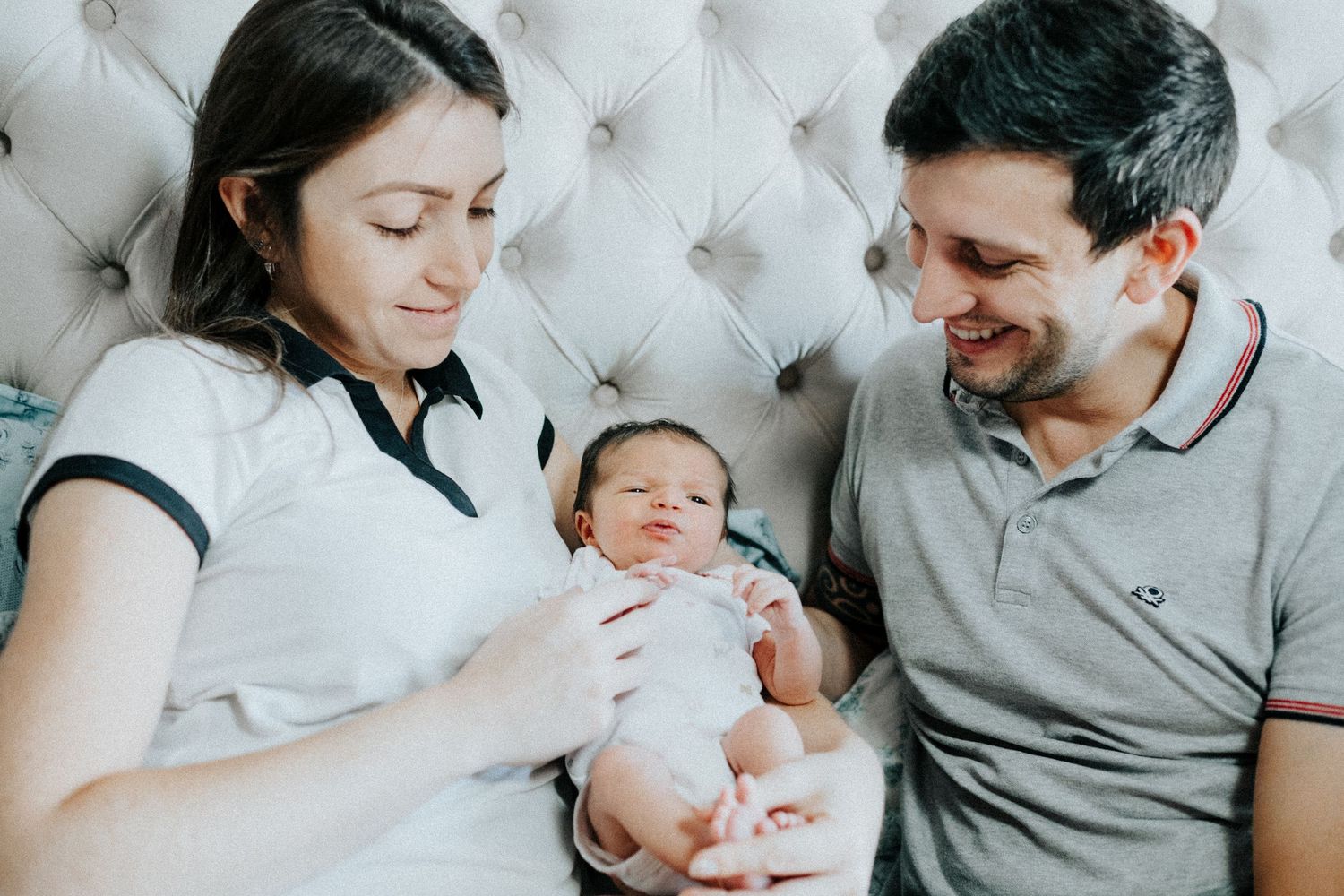 A couple cuddles with their newborn baby on a tufted white couch.
