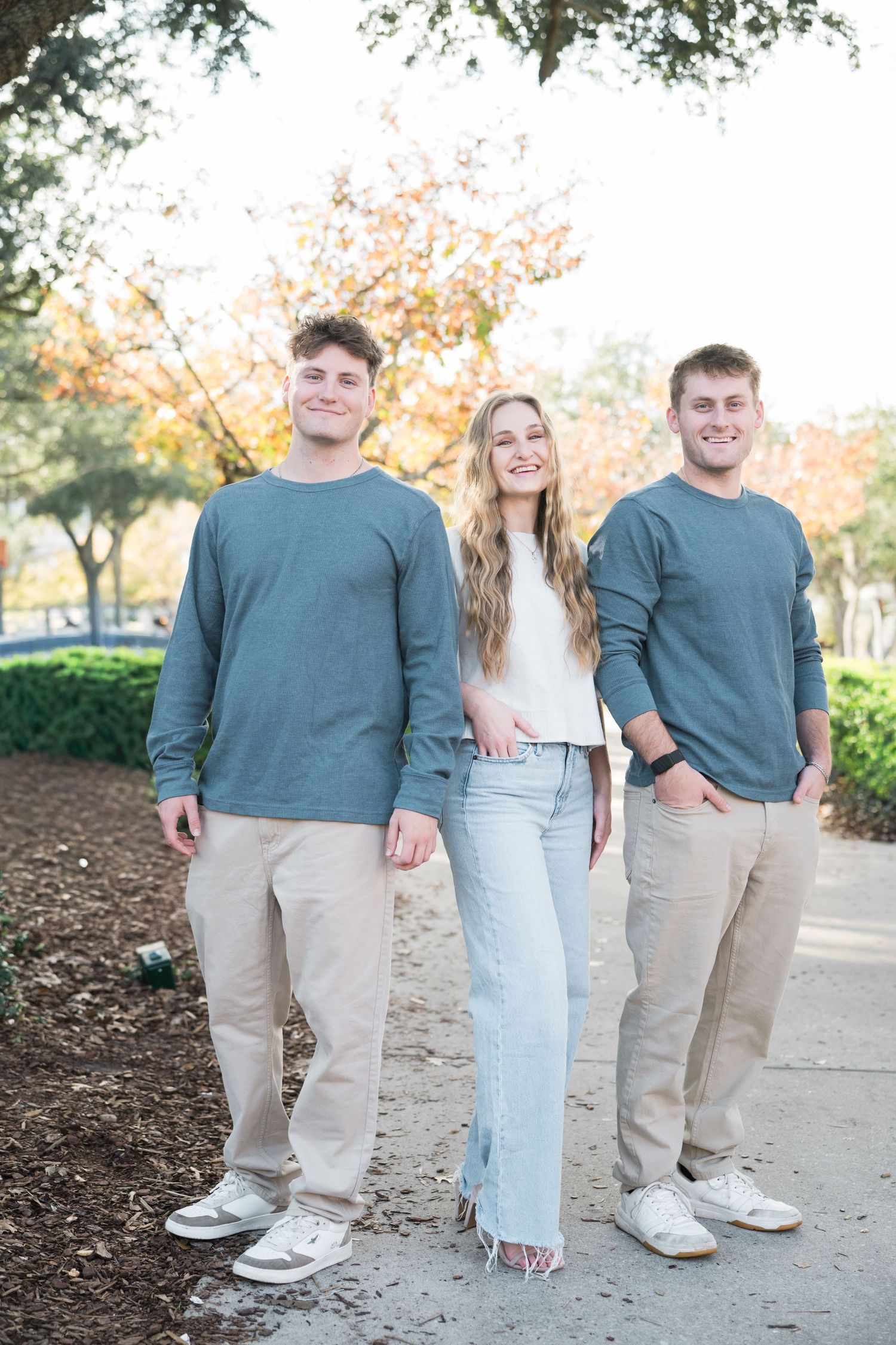 People in coordinated outfits of teal sweaters and khaki pants pose for casual outdoor photos.
