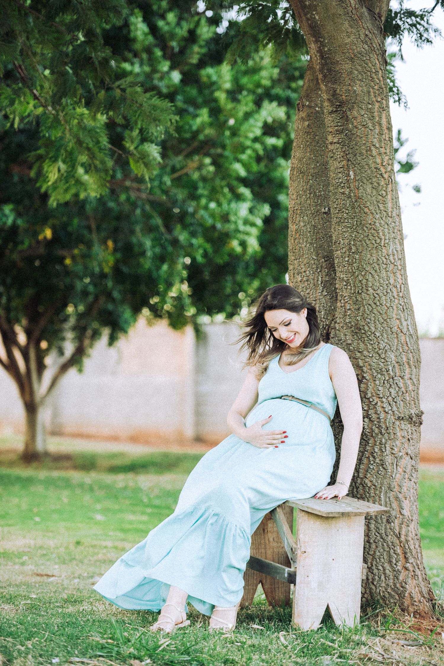 Artistic maternity photos captured near tree trunk in outdoor garden setting.
