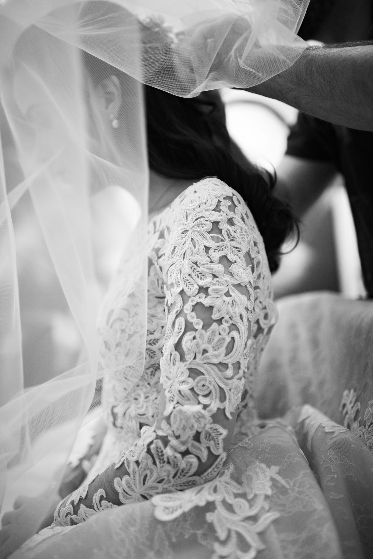 Elegant lace sleeve detail and flowing veil captured in black and white wedding photography.