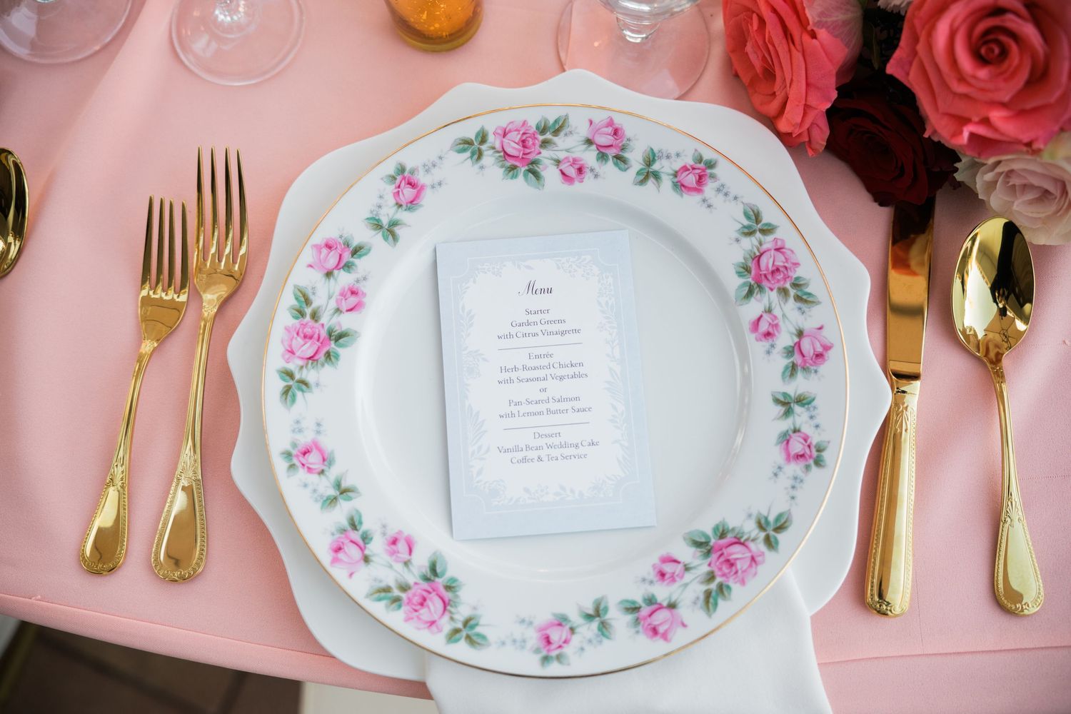 Vintage floral china place settings with gold cutlery on pink tablecloth.