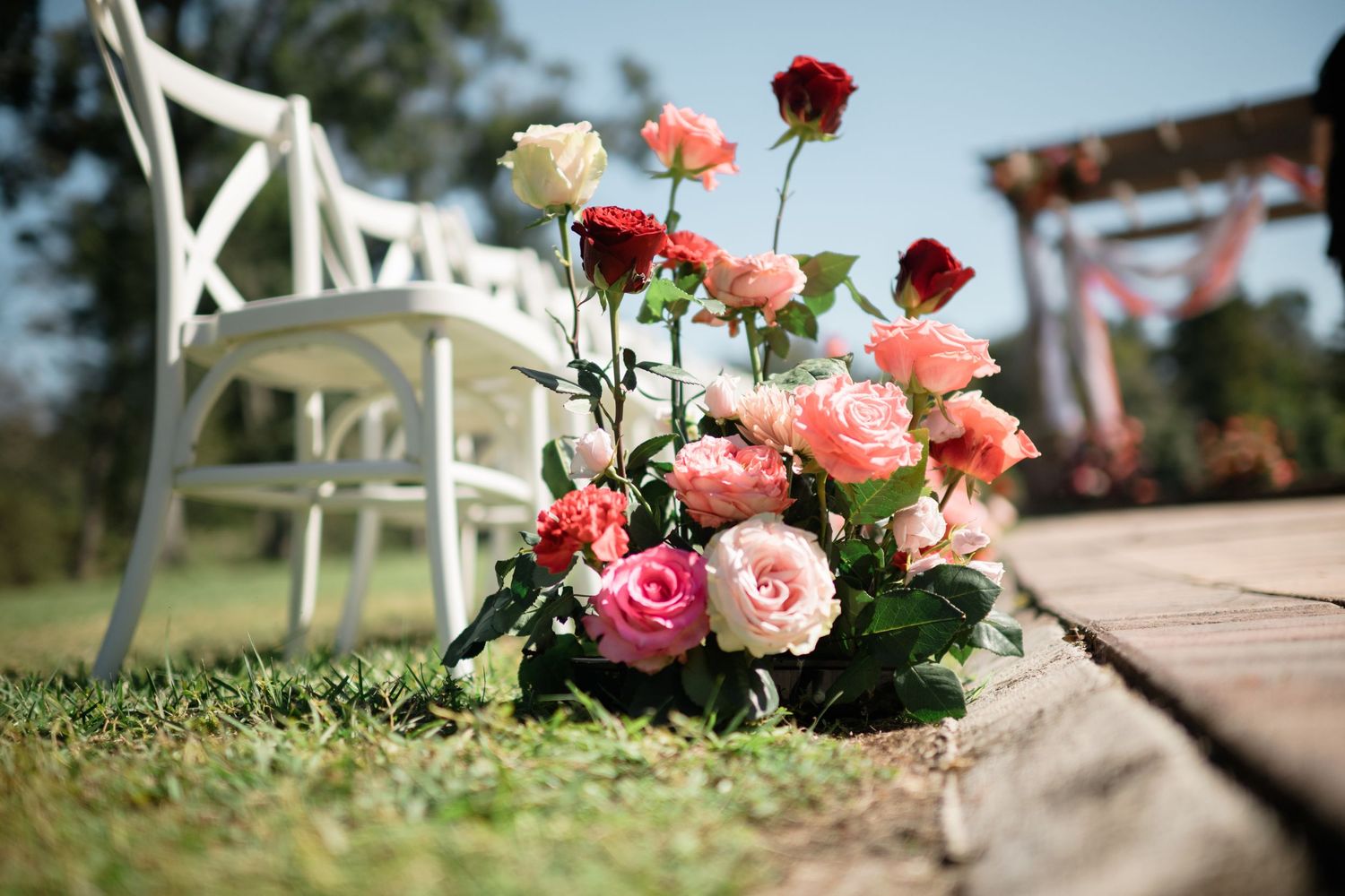 Pink and red roses decorating an outdoor wedding ceremony aisle.