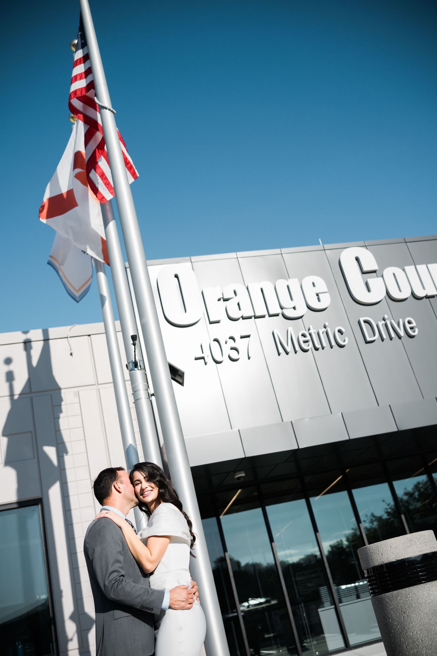 Couple embracing in front of a modern office building with American flags.