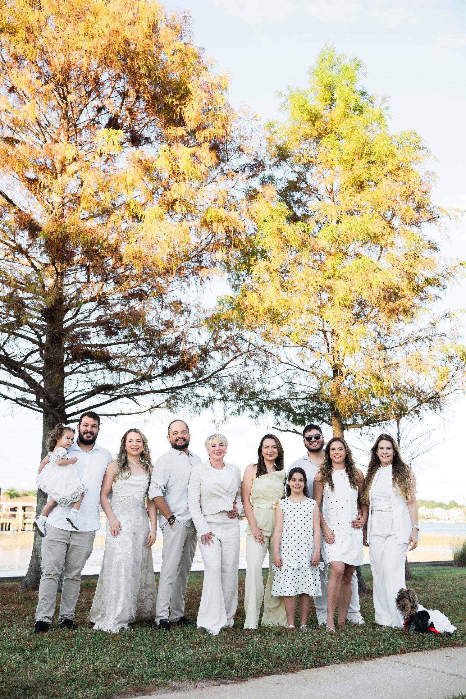 Group wearing white outfits poses together under autumn trees during golden hour.