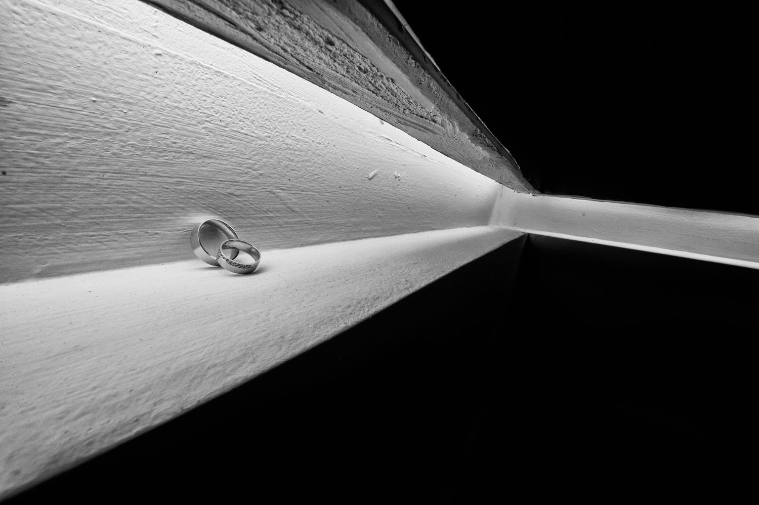 Close-up of wedding rings casting dramatic shadows on a textured white surface.
