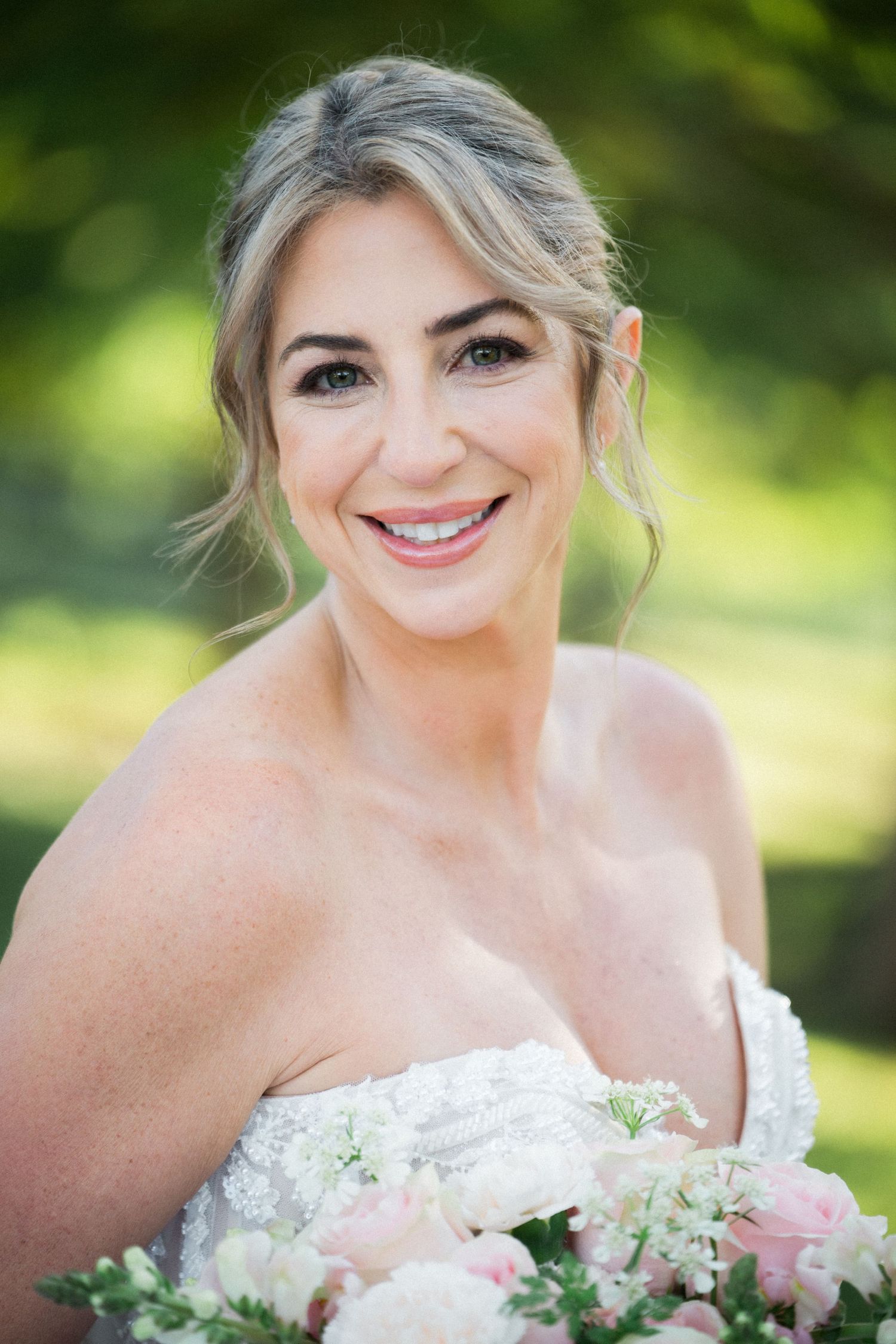 Bridal portrait with white and pink floral bouquet against blurred green background.