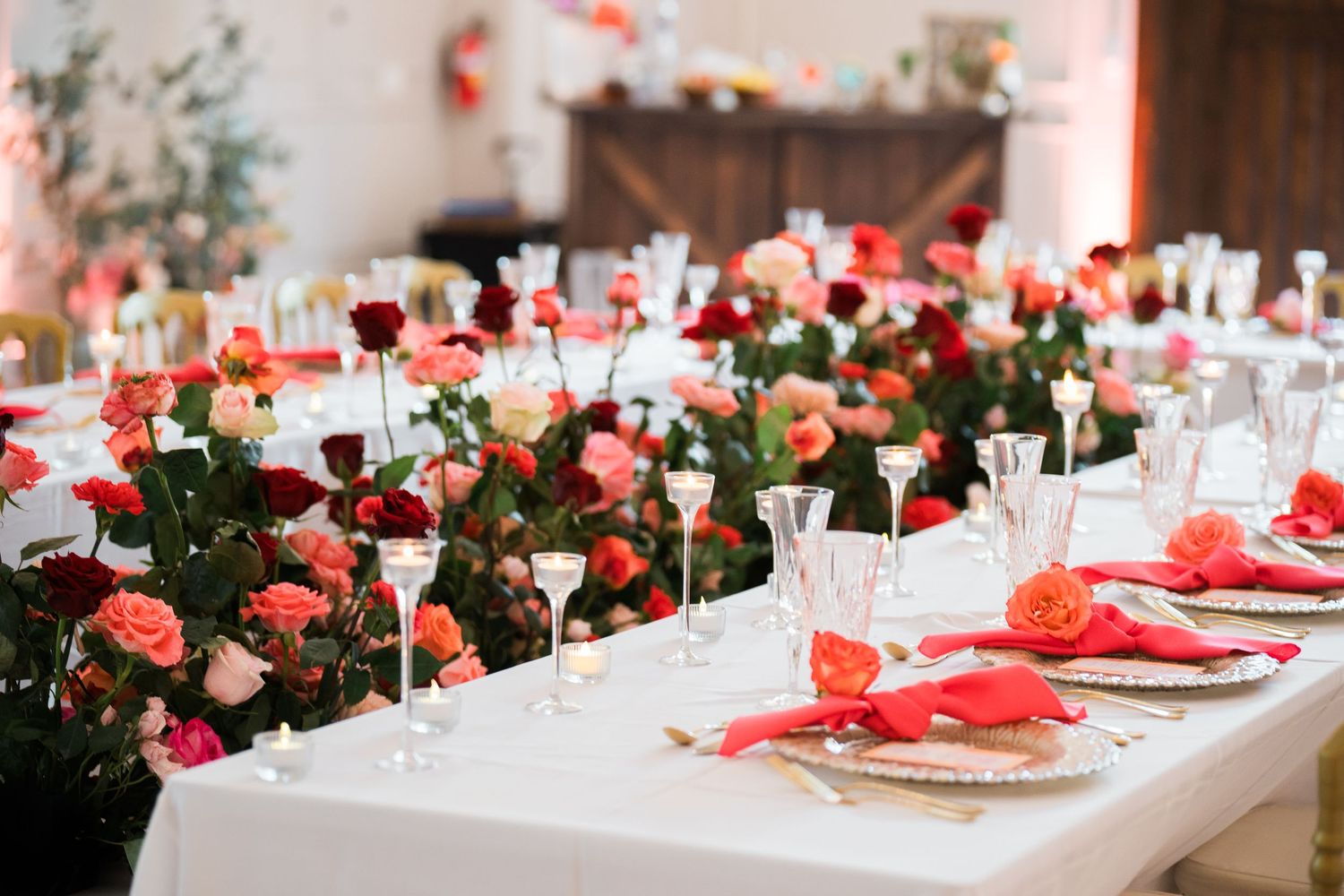 Wedding reception table decorated with red roses, crystal glasses, and white tablecloths.