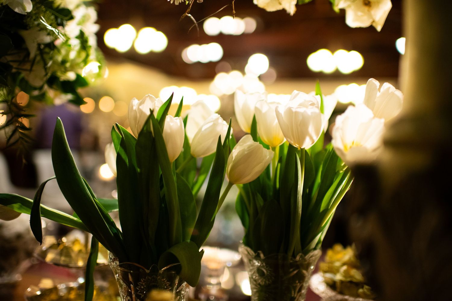White tulips and floral arrangements with bokeh lights creating romantic wedding ambiance.