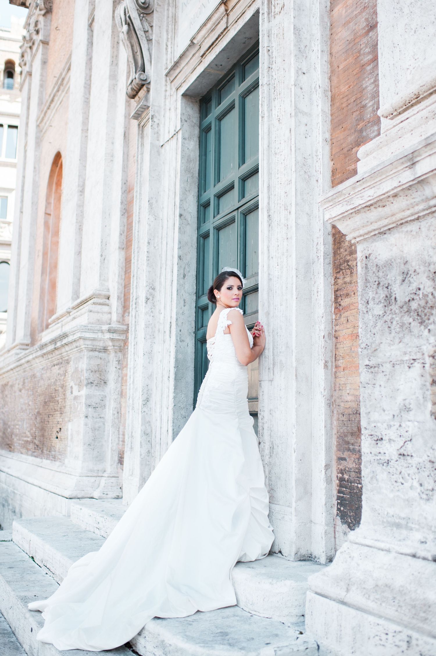 Elegant white wedding dress flowing against weathered stone columns and architecture.