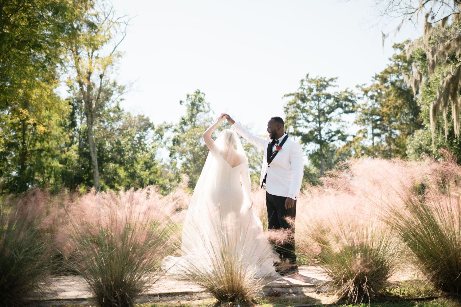 Wedding couple walking through tall ornamental grasses in a garden setting.