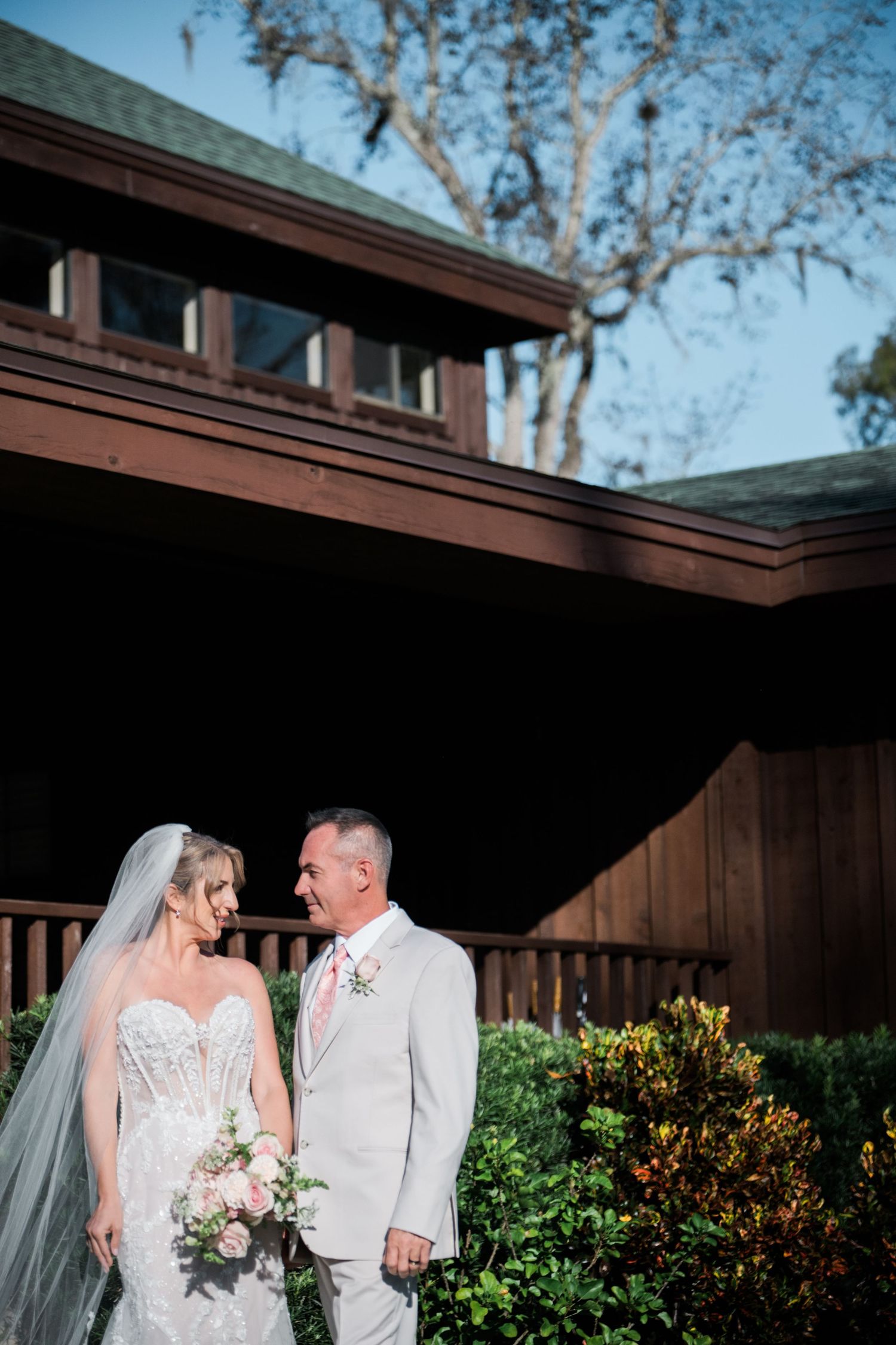 Wedding couple walking together outside a rustic wooden building with landscaping.
