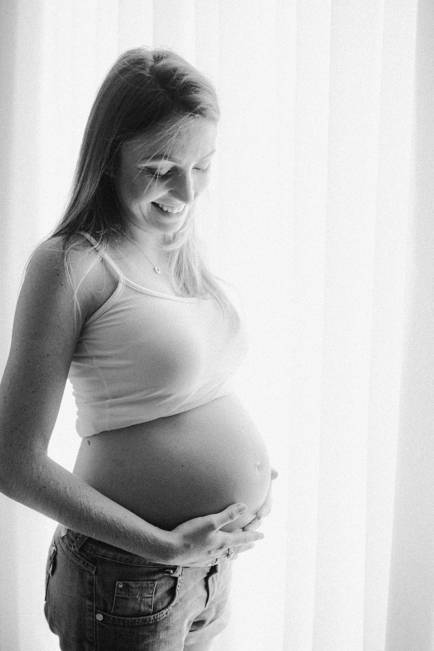 Black and white maternity photo series showing a pregnant woman in white top and jeans against bright background.