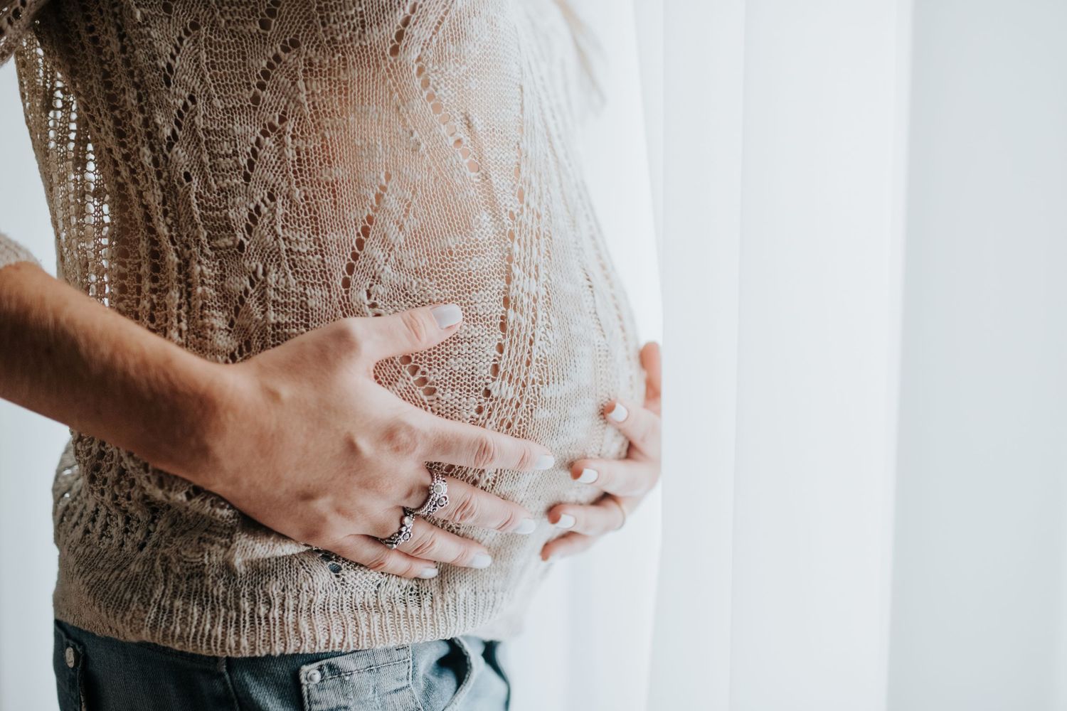 Series of close-up shots showing hands gently cradling a pregnant belly in beige sweater.
