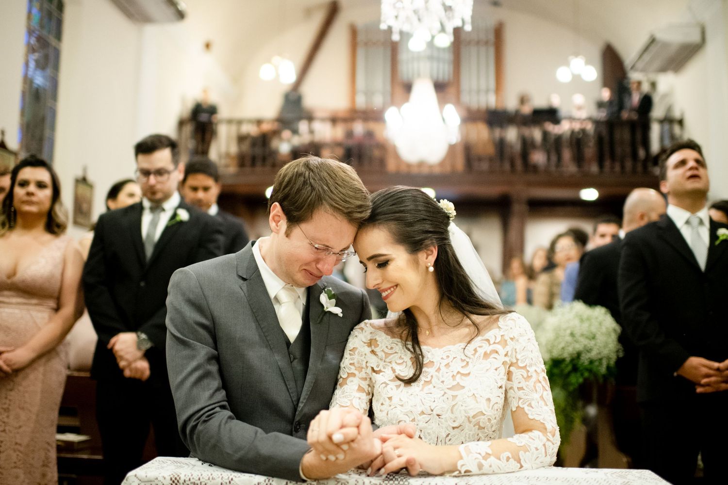 Tender moment shared during wedding ceremony in church with chandelier overhead.