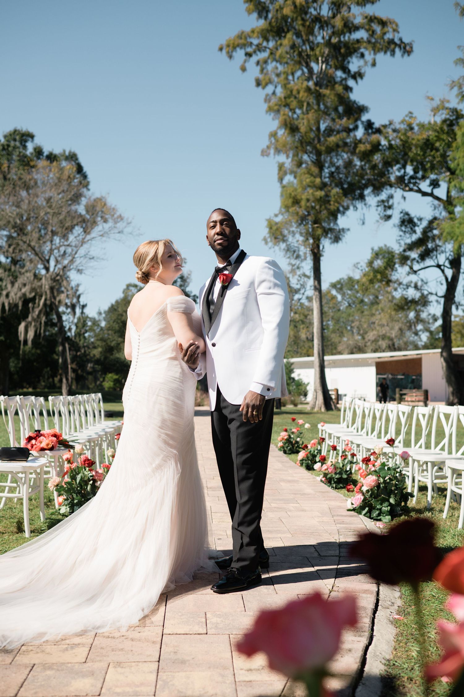 Outdoor wedding portraits on a stone pathway with white chairs and floral decorations.