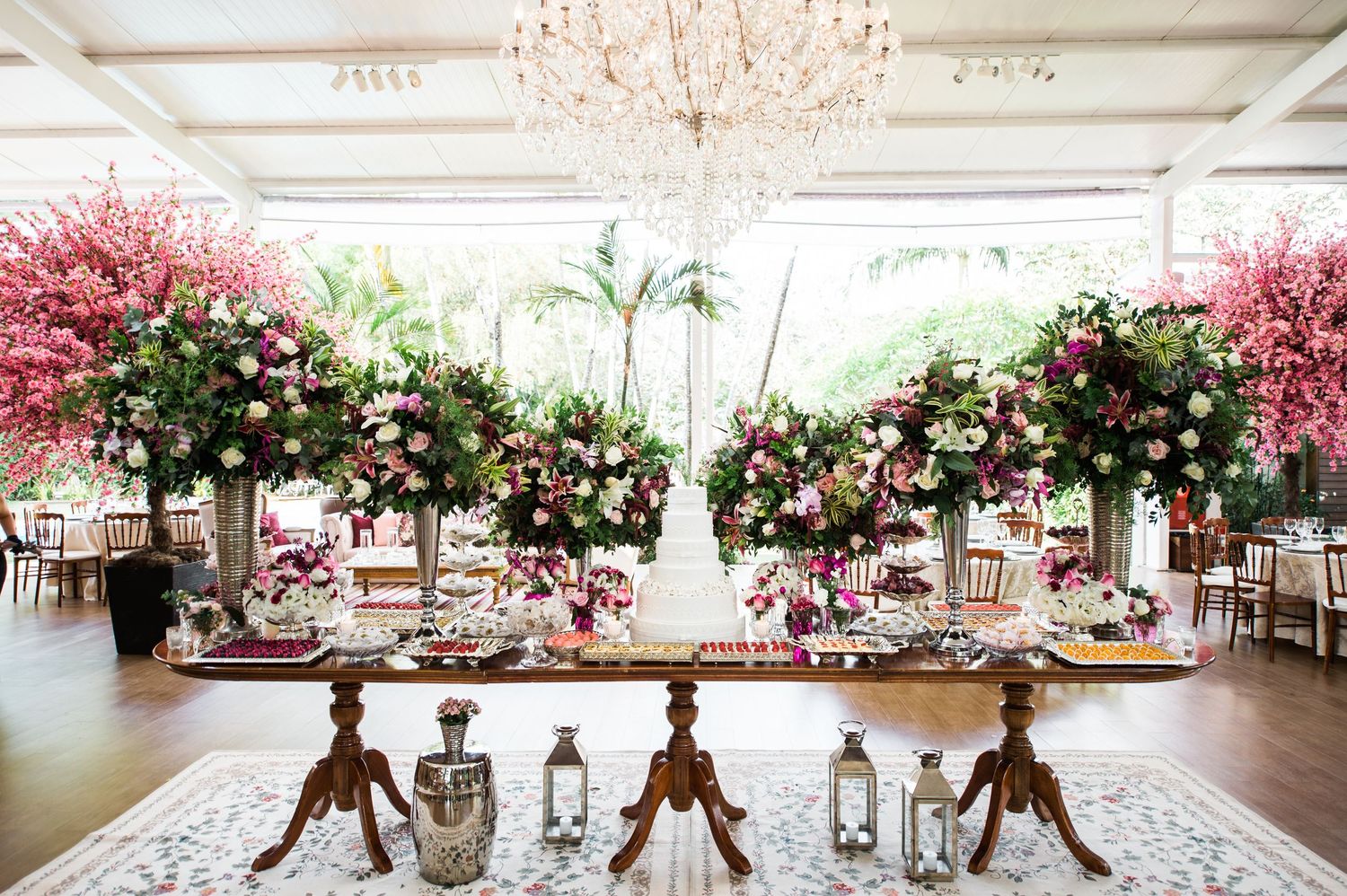 Elegant reception hall with crystal chandelier and pink floral arrangements on round tables.