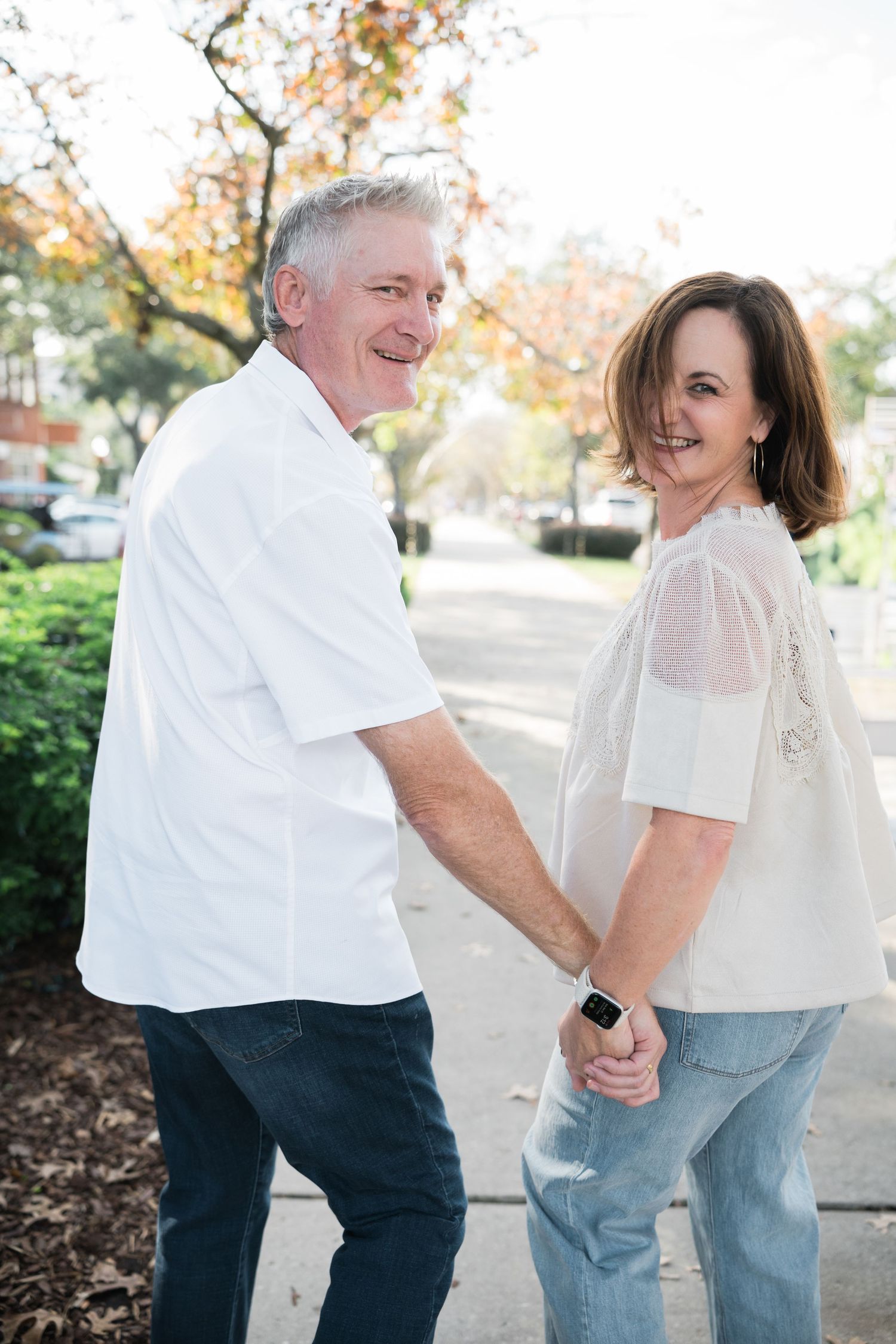 Playful couple in coordinated white and denim outfits laughing together outdoors.