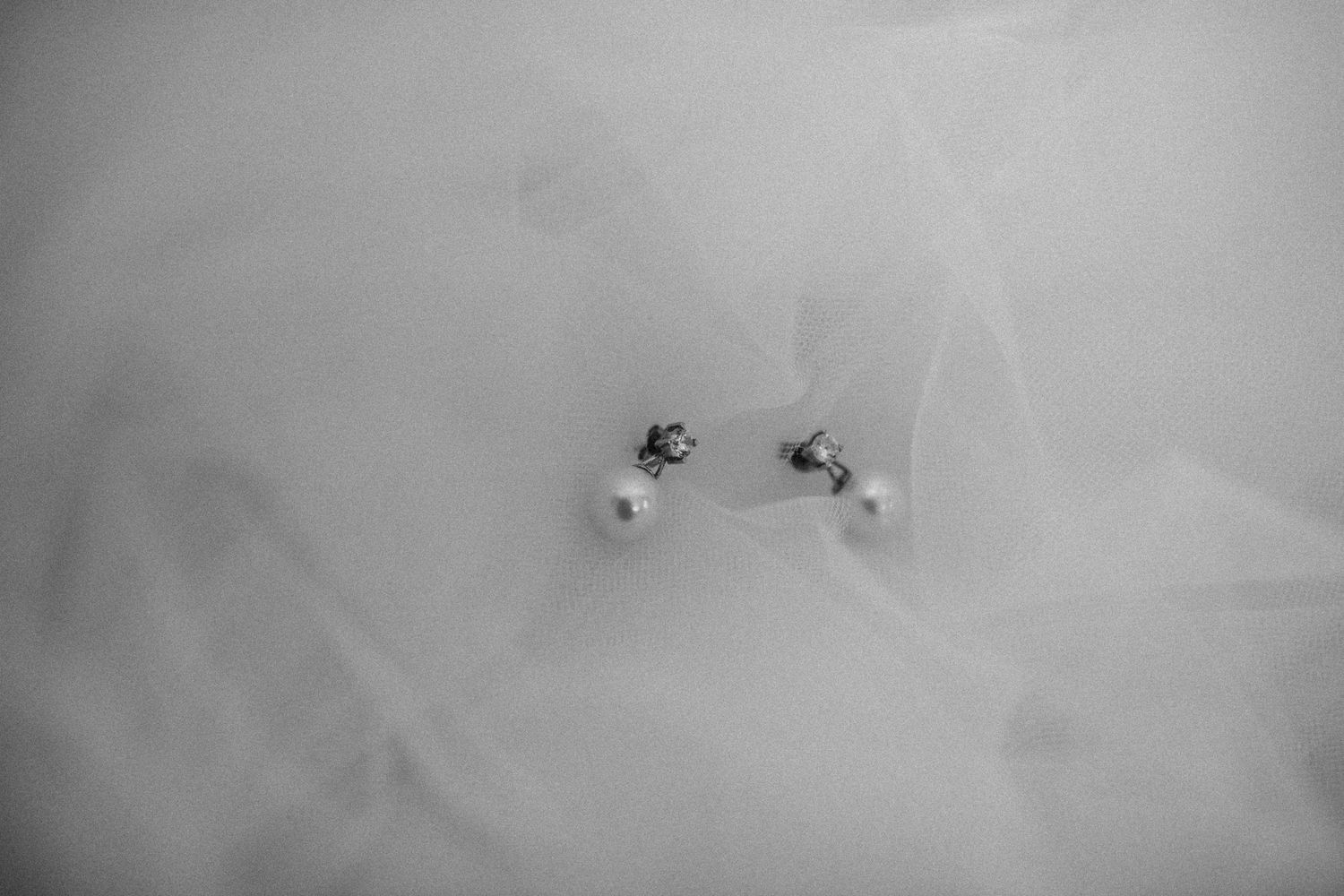 Delicate pearl earrings photographed against soft white fabric.