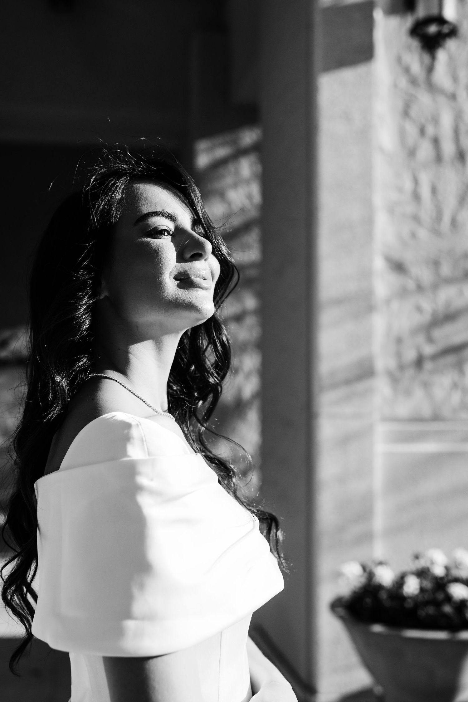 Dramatic black and white portrait of woman in white dress against stone wall.