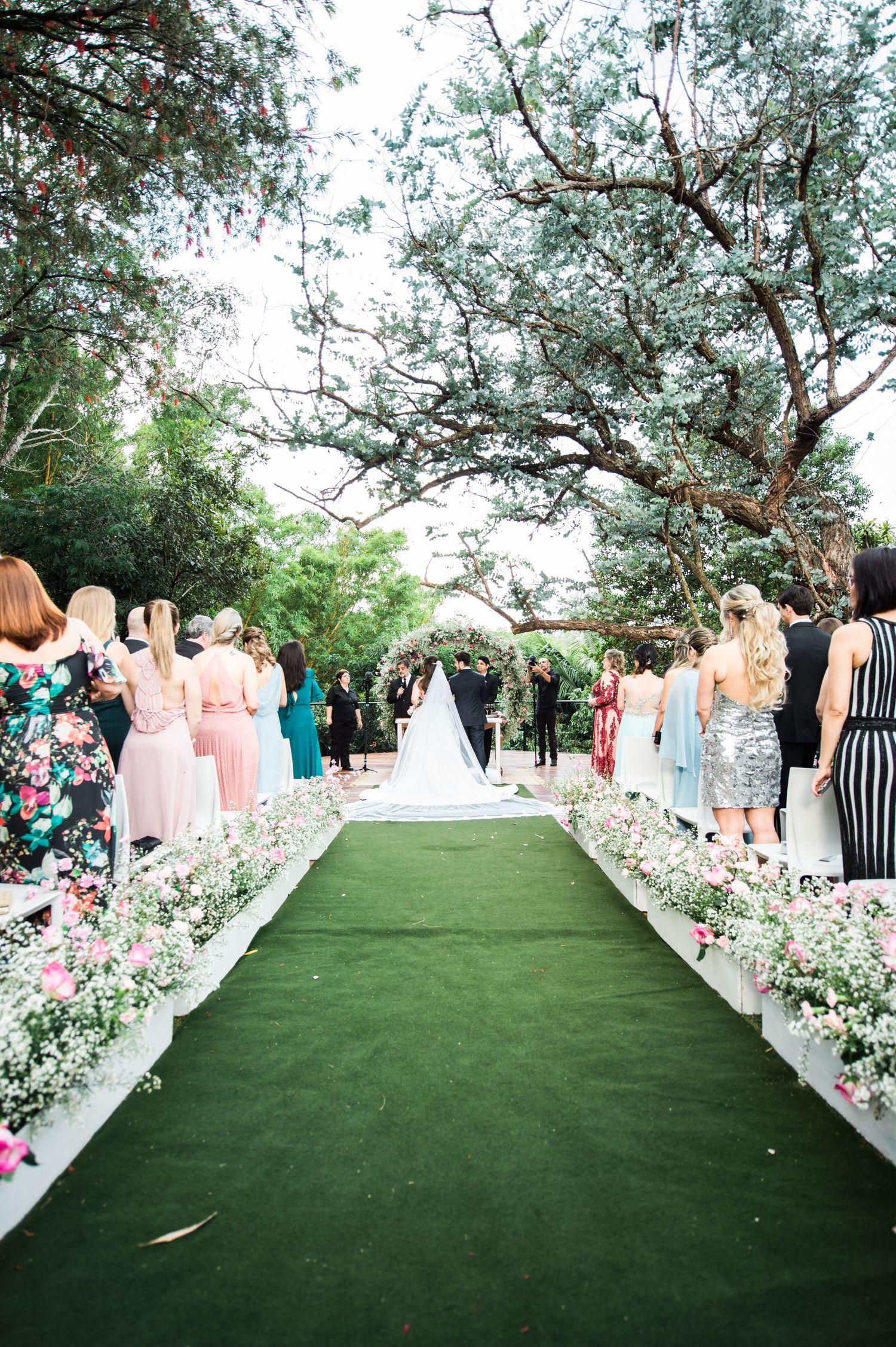Wedding ceremony aisle decorated with white flowers and greenery on artificial turf.