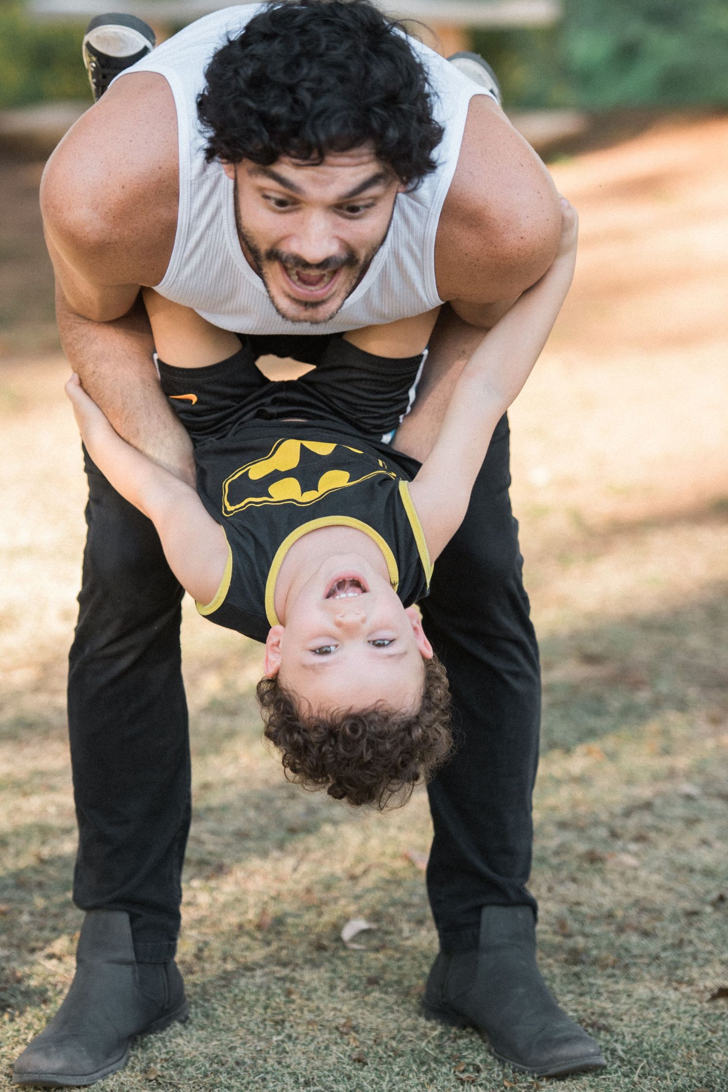 Playful sequence showing someone holding a child upside down while playing outdoors.