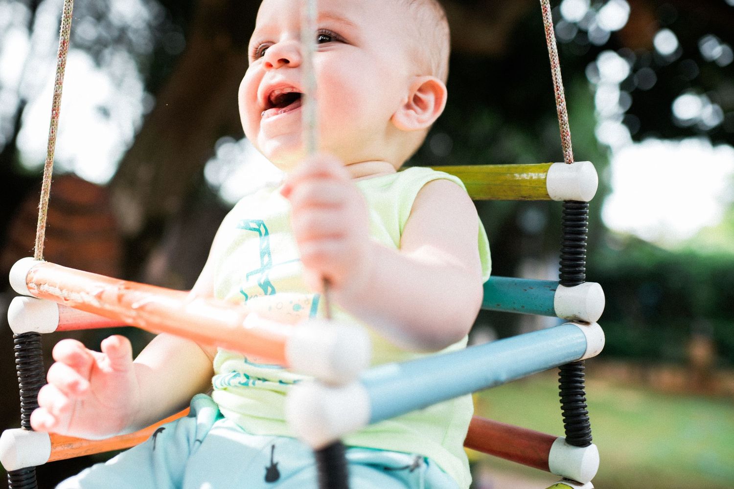 Baby playing on outdoor playground equipment with bright bokeh lights in background.