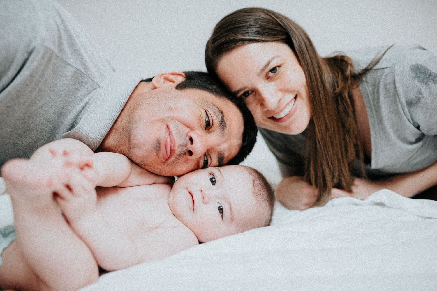 Mother and baby share tender moment while lying on white bedding.