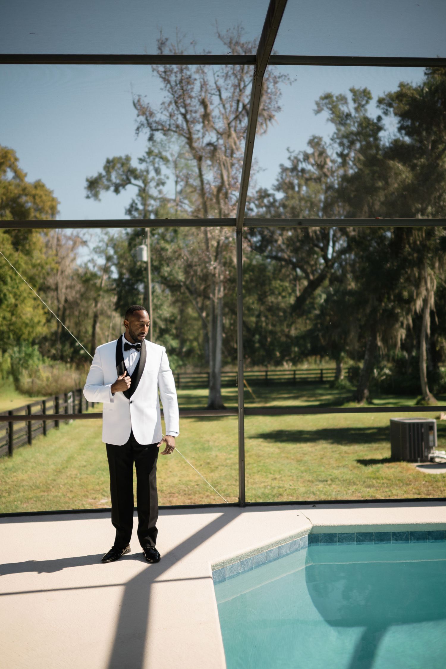 Person in formal white tuxedo standing by modern swimming pool.