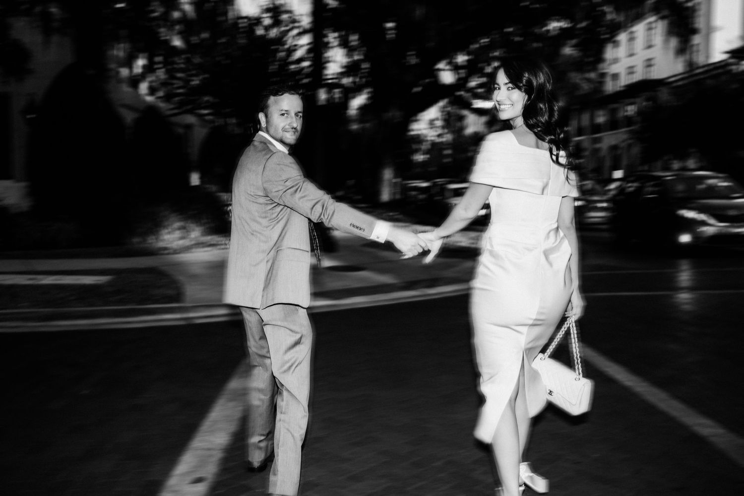 A black and white photo of a couple holding hands while walking outdoors.