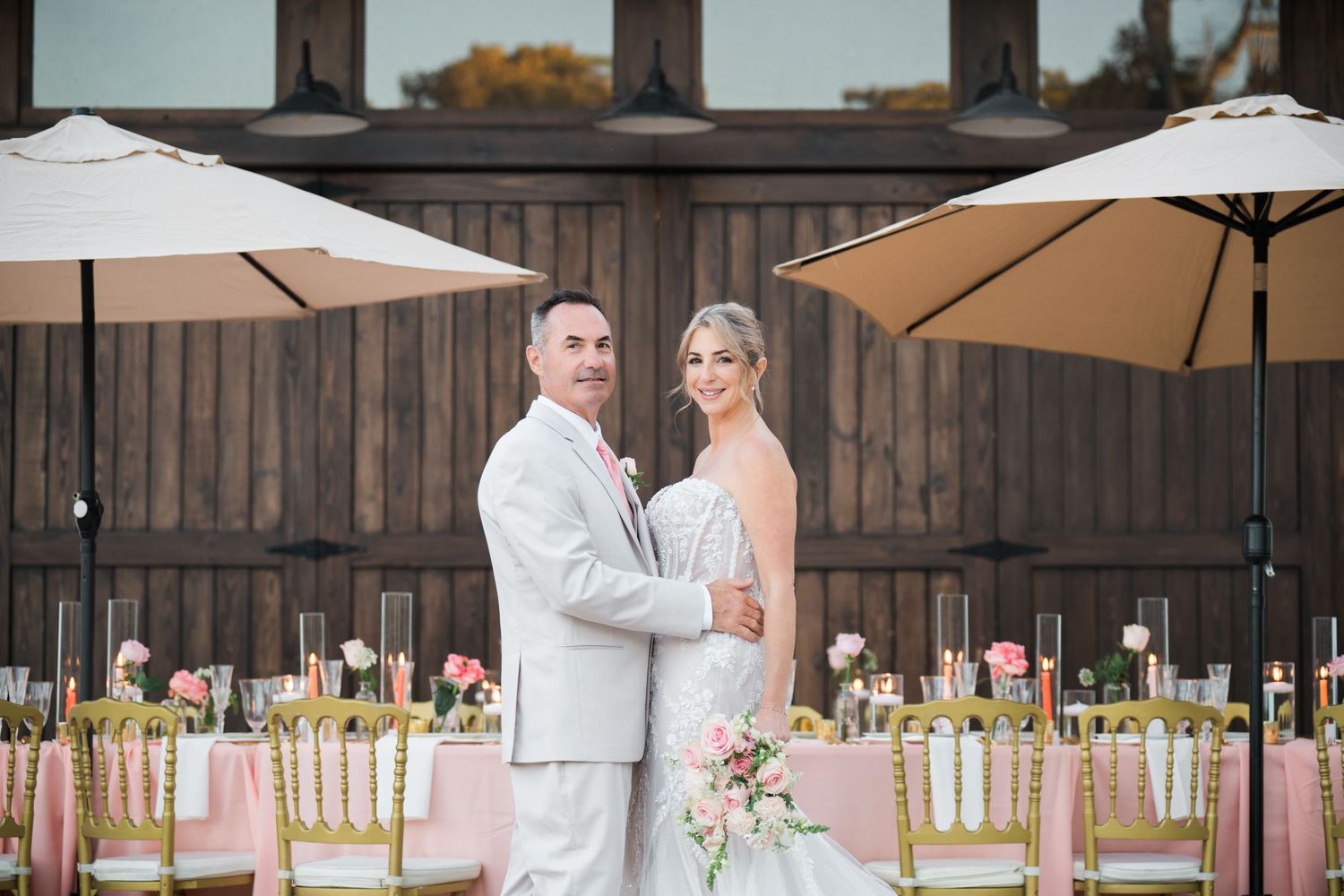 Wedding reception setup with gold chairs and table settings under outdoor umbrellas.
