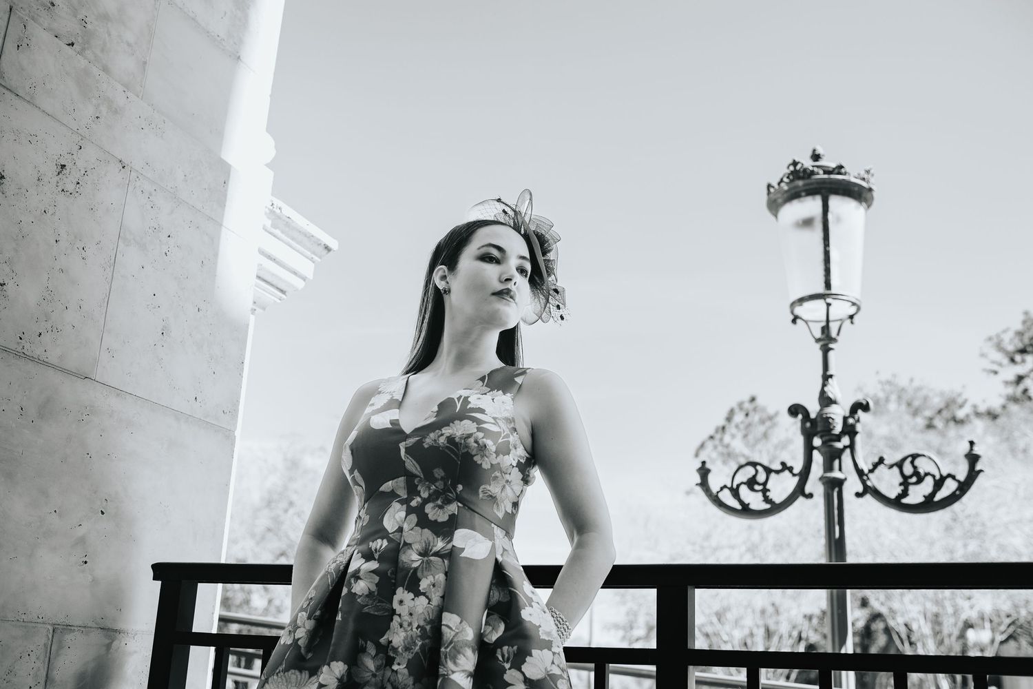 Black and white portrait of woman in floral dress posing by vintage lamp post.