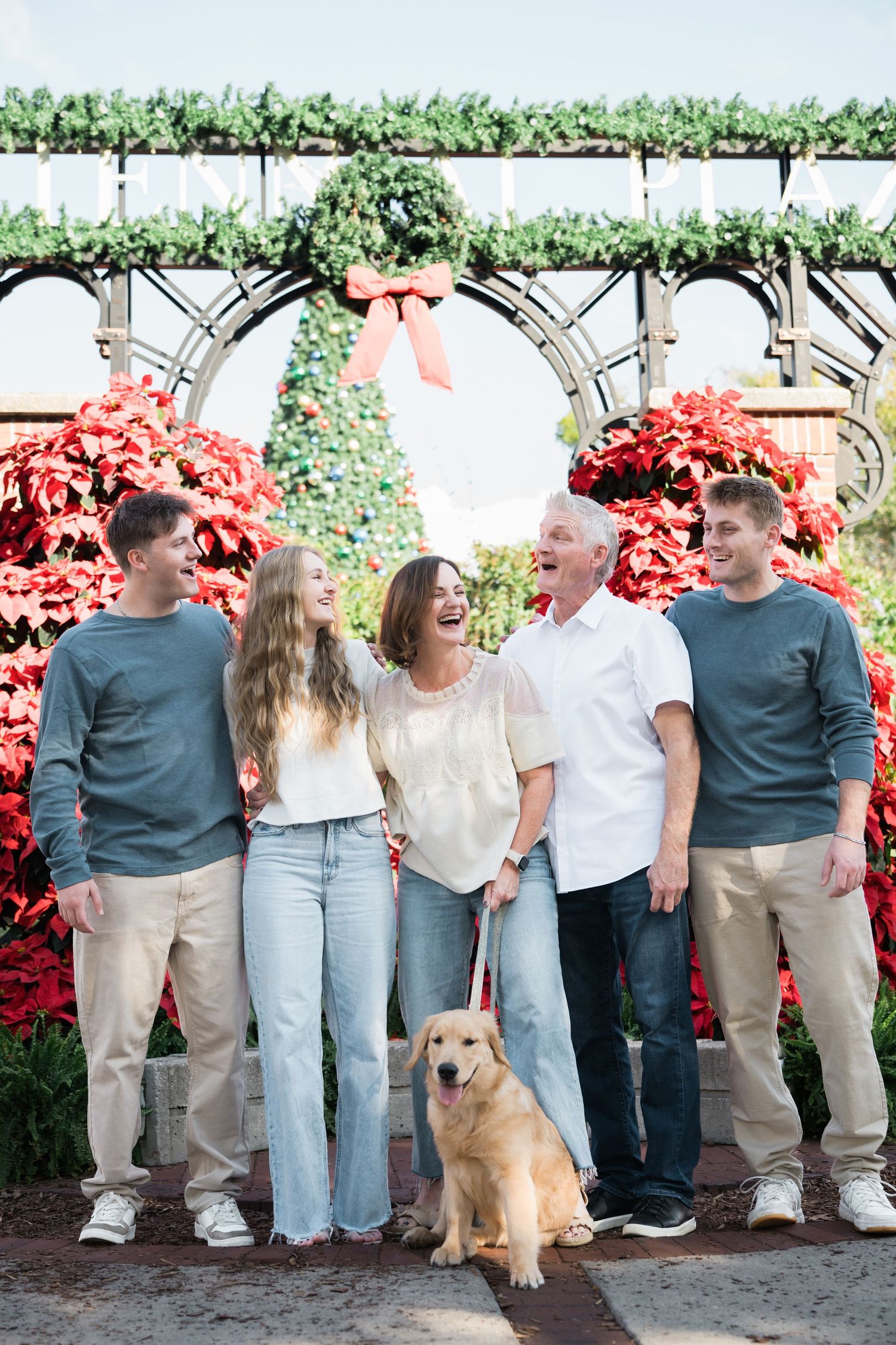 Family group with golden retriever poses together against flowering bushes.