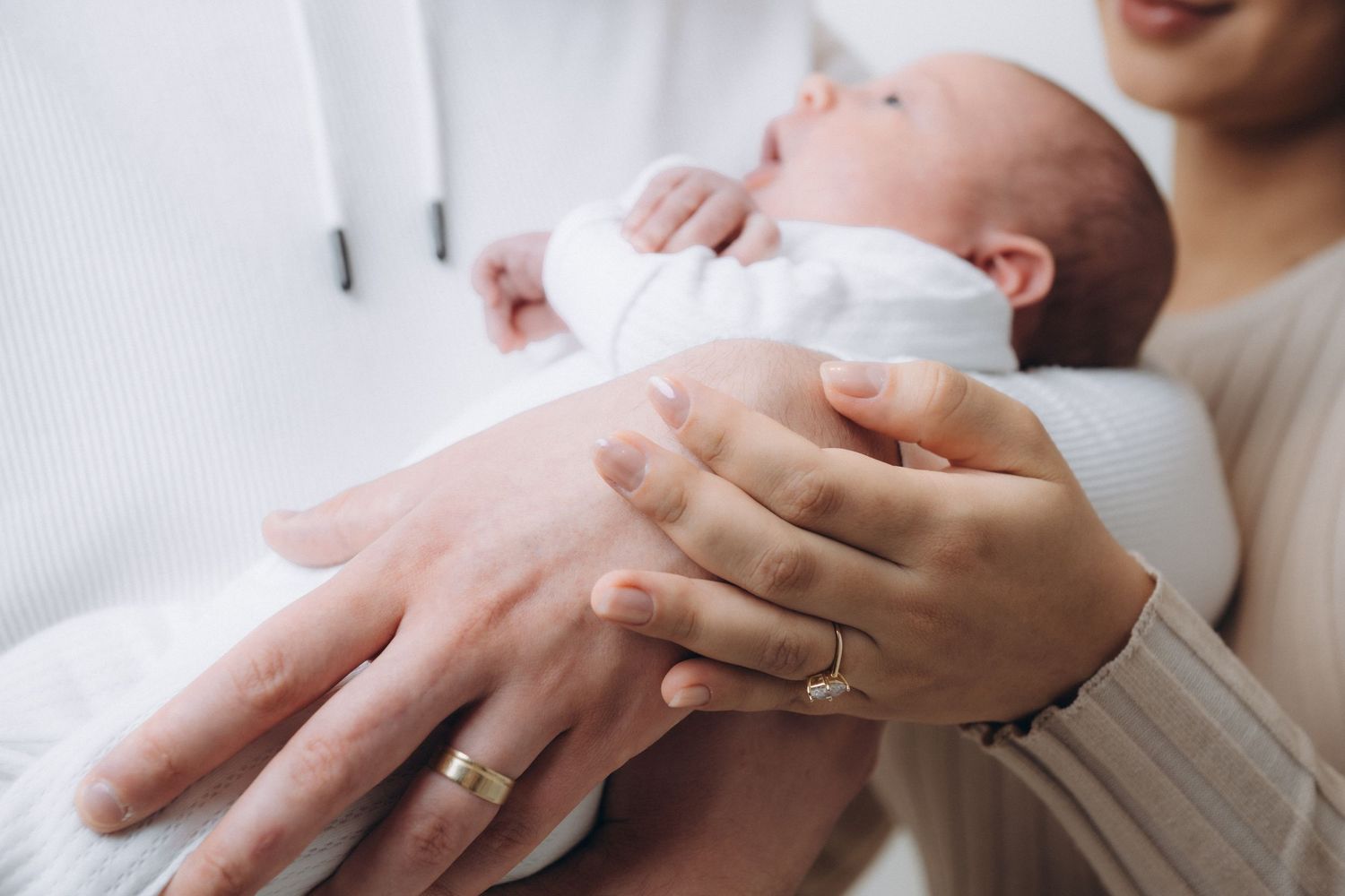 Close-up of hands gently cradling newborn baby wrapped in white.