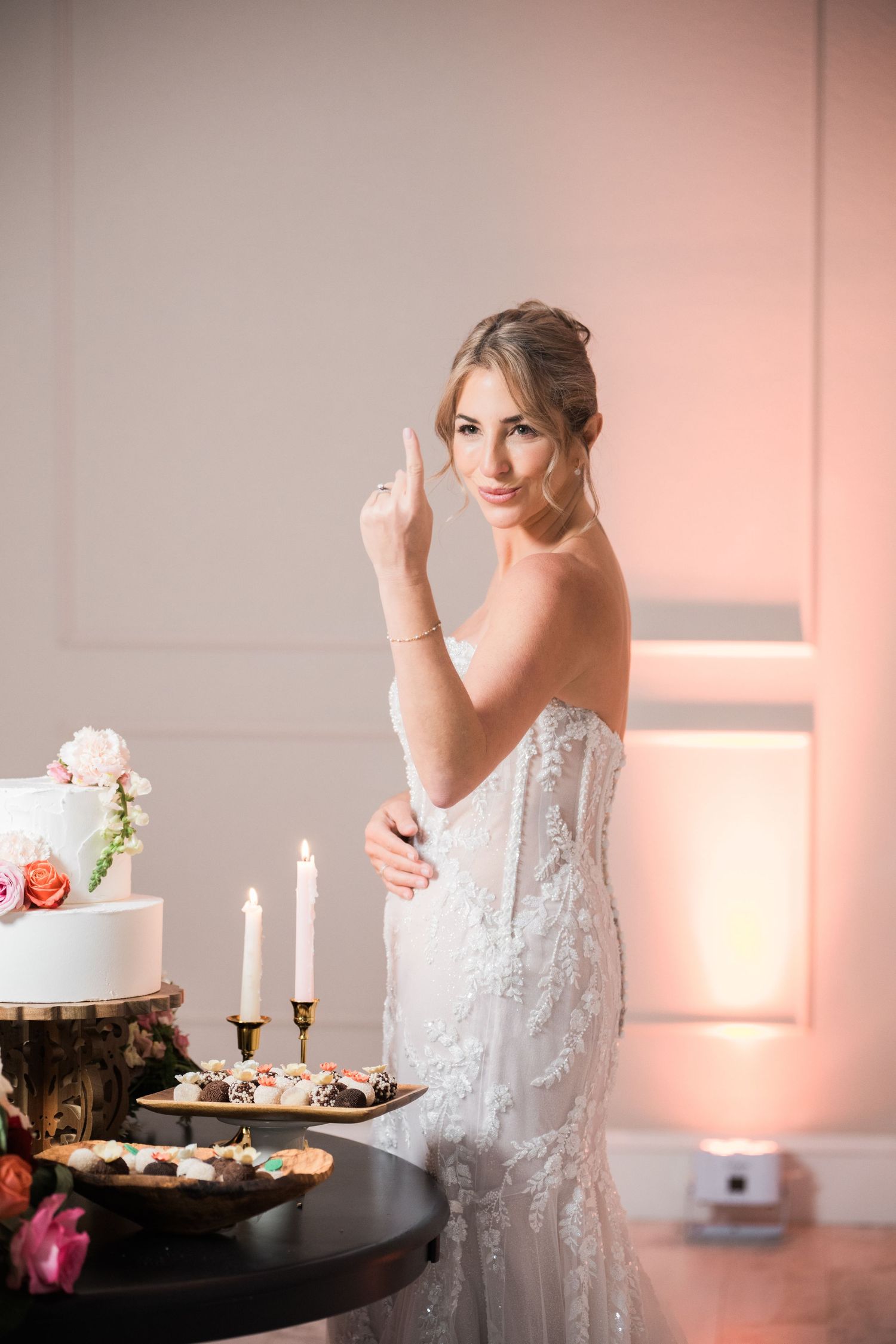 Romantic wedding dessert table setup with pink florals and white candles creating an intimate atmosphere.