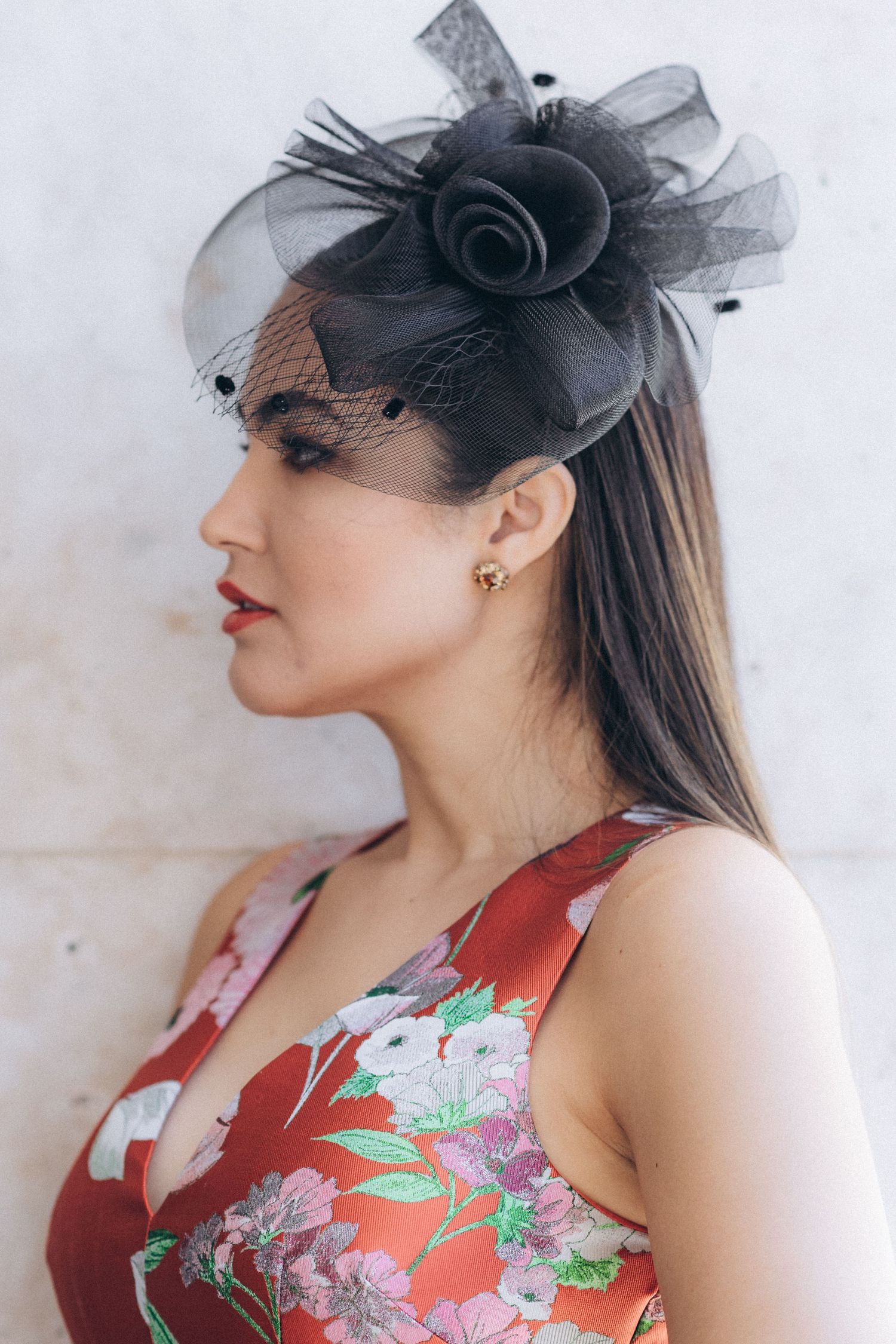 Side profile of woman wearing black fascinator and red floral dress.
