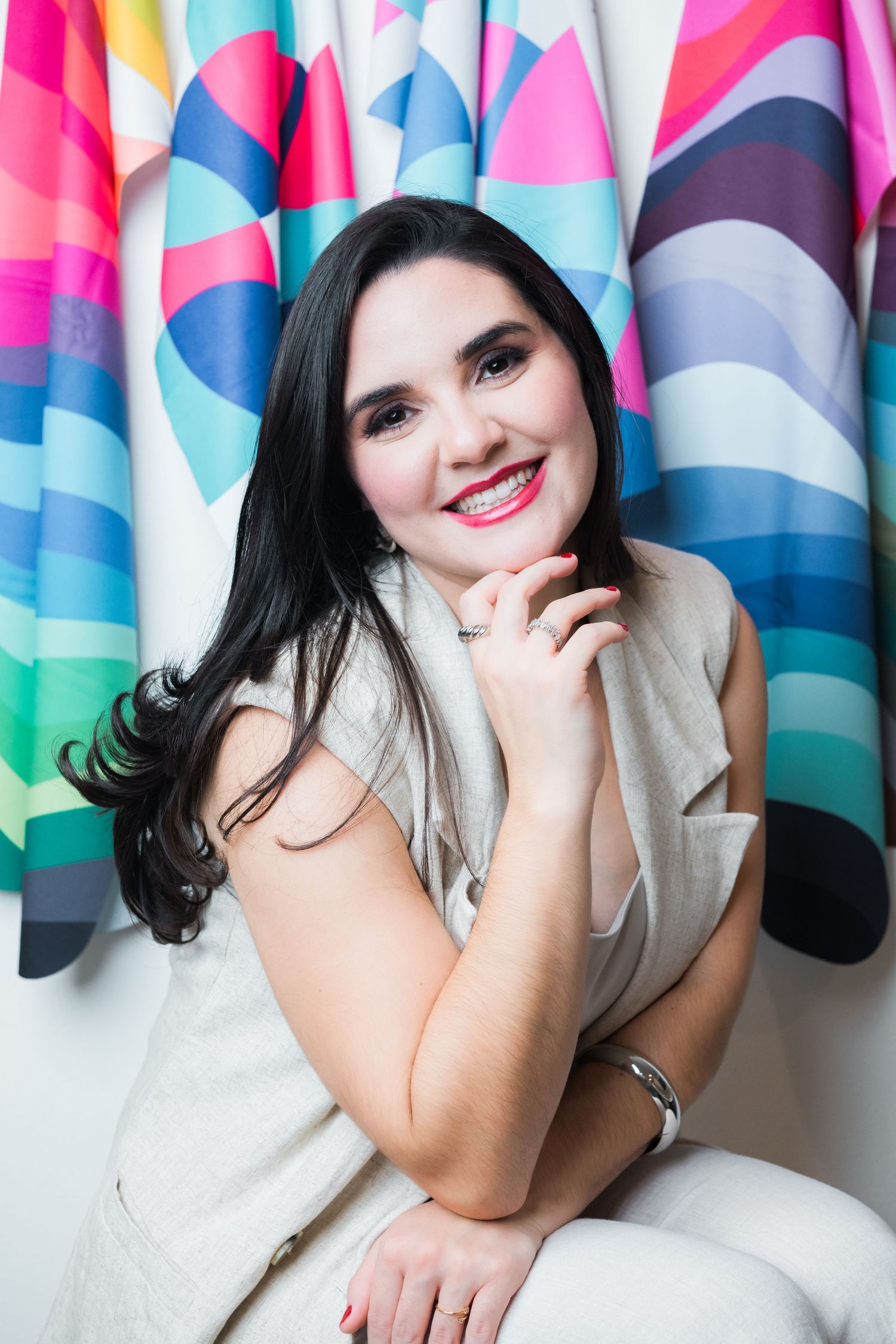 Smiling woman in white dress poses against colorful geometric patterned backdrop during photo session.