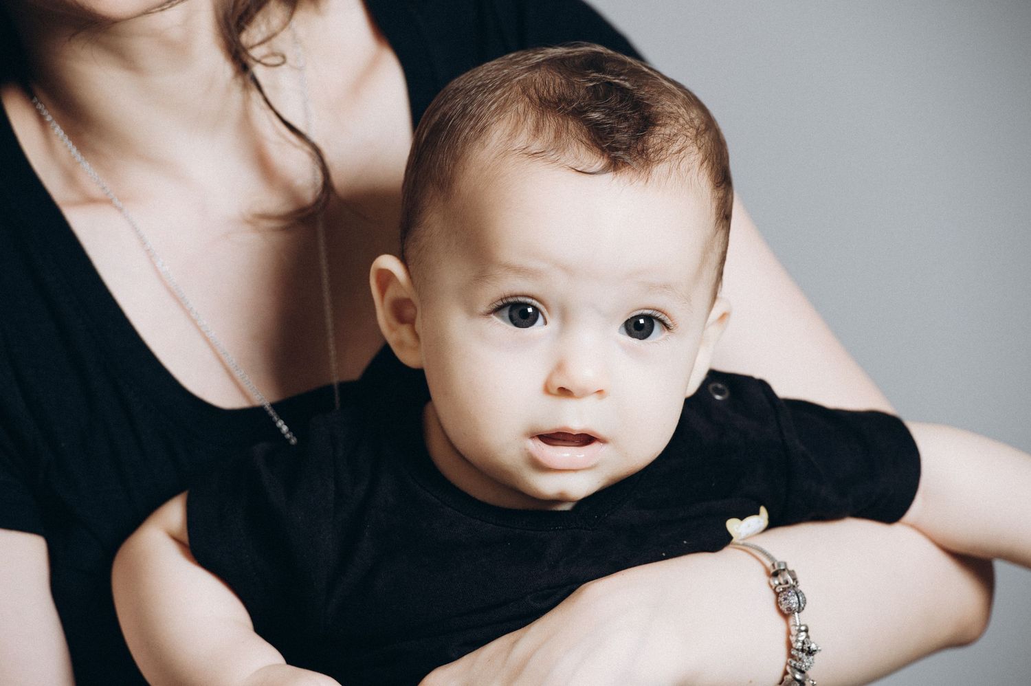 Close-up studio portrait of a baby with bright eyes in dark clothing.