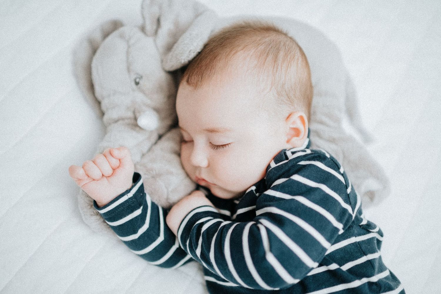 Infant naps peacefully wearing navy striped outfit on soft gray blanket.