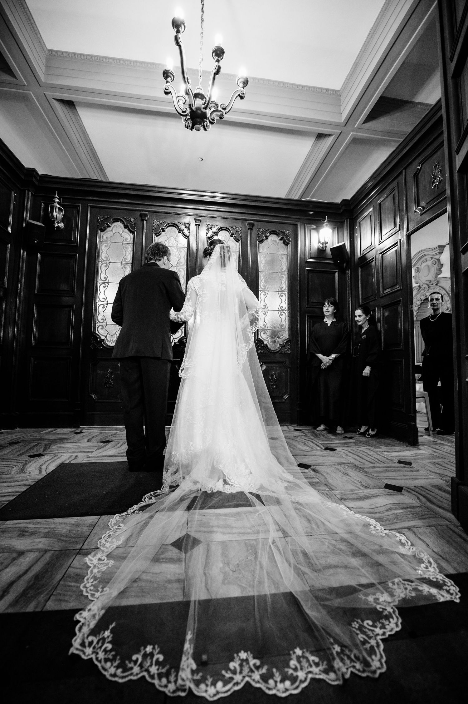 Elegant wedding dress with intricate lace train displayed in grand ballroom setting.