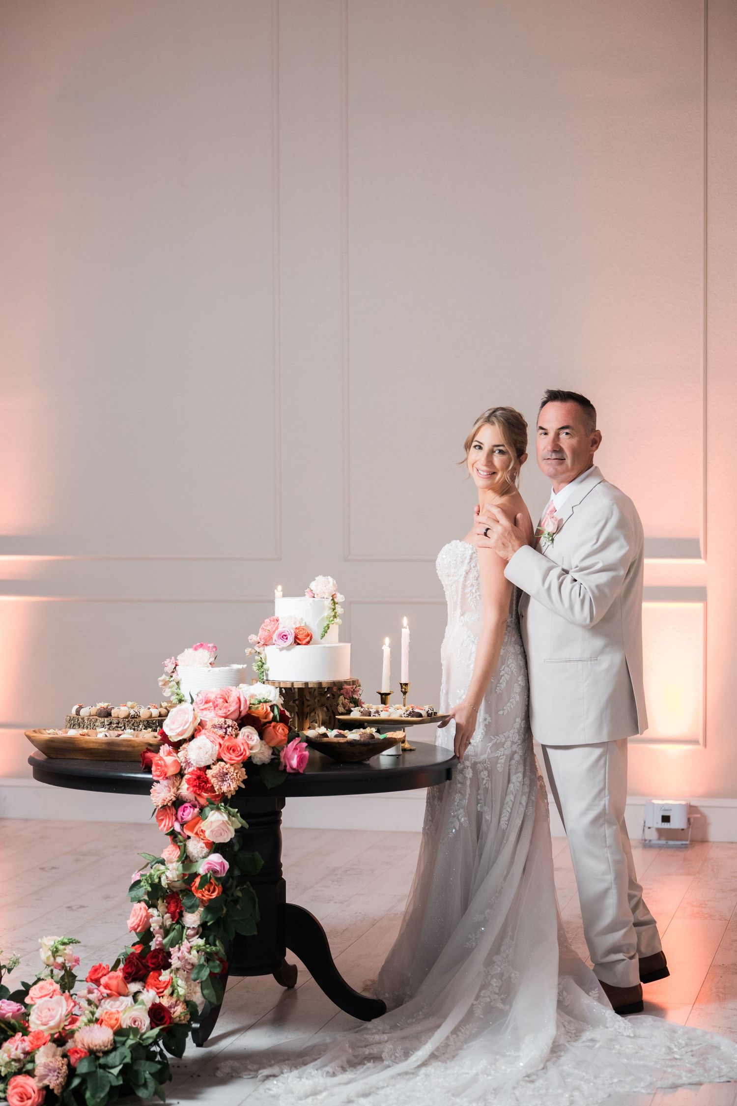 Couple in wedding attire playfully posing near an elegantly decorated dessert table.