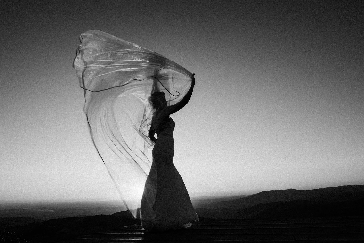 Dramatic black and white silhouettes against sunset sky with flowing fabric.